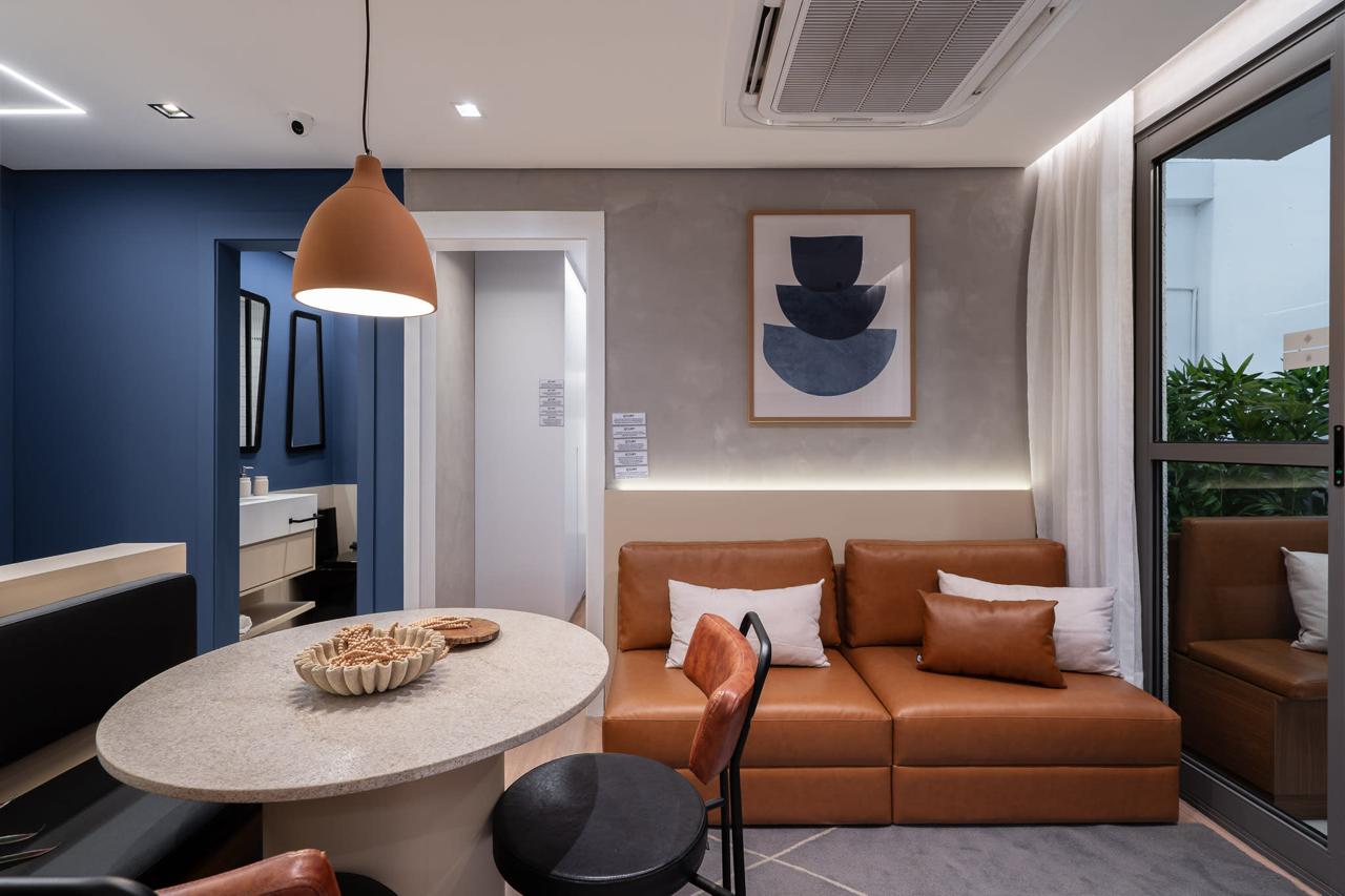 Sala de jantar e cozinha integradas com mesa redonda e cadeiras, banco embutido e pendente central, ao lado de armários claros e bancada com pia, em apartamento moderno de tons neutros com clima acolhedor e organizado